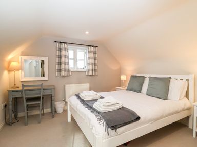 A bedroom with a bed with pillows and towels a desk with a chair and a window with curtains at 2 Mosses Cottage in Friston