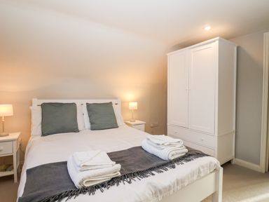 A bedroom with a bed, two bedside tables with lamps, and a white wardrobe at 2 Mosses Cottage in Friston