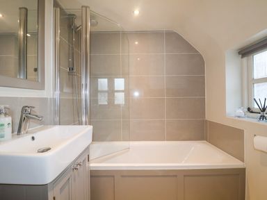 A bathroom with a bathtub and shower beside a sink and a window at 2 Mosses Cottage in Friston