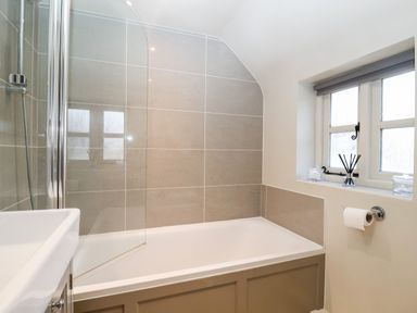A bathroom with a bathtub shower combination next to a window at 2 Mosses Cottage in Friston