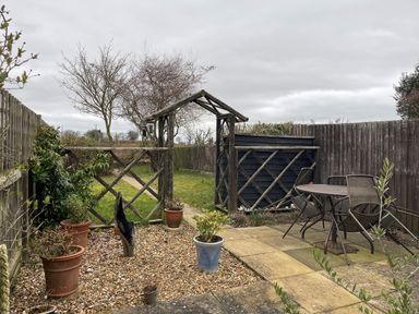 A backyard with potted plants gravel area wooden arch gate patio table and chairs and fenced garden at 2 Mosses Cottage in Friston