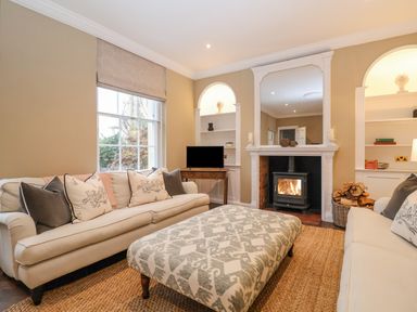 A living room with two sofas a patterned ottoman a fireplace with a wood burning stove and built in shelves at The Middle House in Southwold