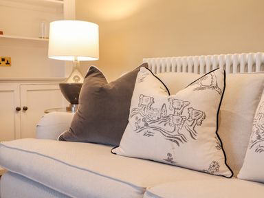 A beige sofa with decorative pillows and a table lamp on a side table at The Middle House in Southwold
