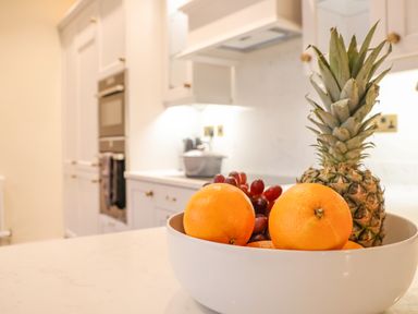 A kitchen with a white bowl containing oranges pineapple and grapes on a countertop at The Middle House in Southwold