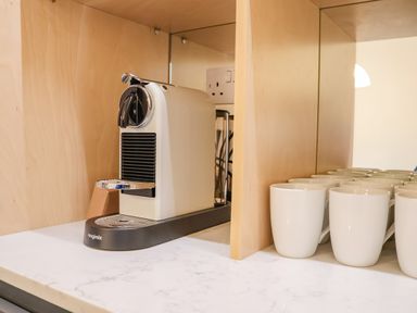 A coffee machine and white mugs on a marble countertop with wooden panel walls at The Middle House in Southwold