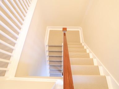 A staircase with beige carpet and wooden handrail with white walls at The Middle House Southwold