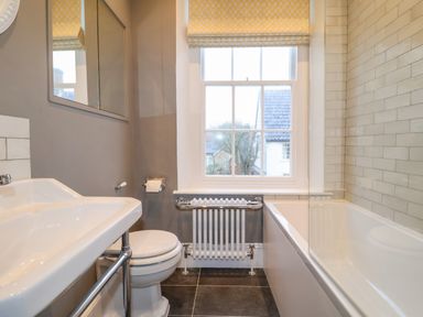 A bathroom with a sink toilet radiator and bathtub under a window at The Middle House in Southwold