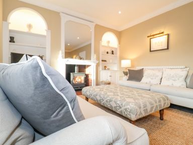 A living room with sofas an ottoman a fireplace and shelves at The Middle House in Southwold