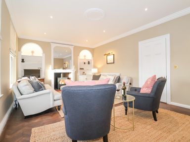 A living room with sofas armchairs a fireplace and a small round table with a wine bottle at The Middle House in Southwold