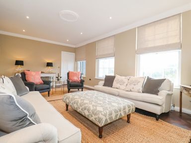 A living room with sofas armchairs a patterned ottoman and a jute rug at The Middle House in Southwold