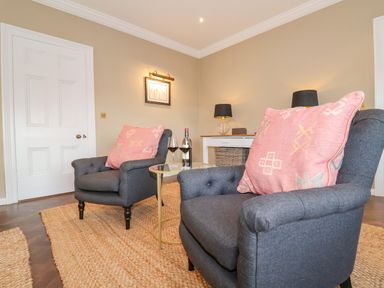 A sitting area with two gray armchairs with pink cushions and a small round table with wine glasses and bottle at The Middle House in Southwold