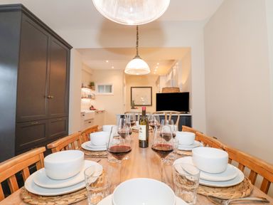 A dining room with set table and wine glasses in front of a kitchen at The Middle House in Southwold