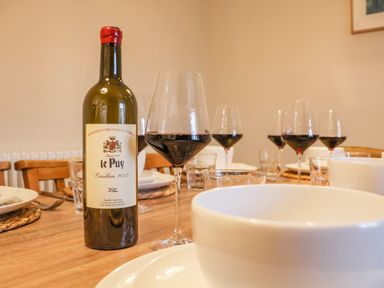 A dining table set with a bottle of red wine glasses plates and bowls at The Middle House in Southwold