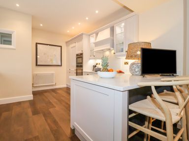 A kitchen with a white countertop island fruit bowl wicker lamp chairs and a wall-mounted oven at The Middle House in Southwold