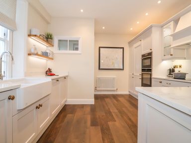 A kitchen with white cabinets wooden floor and built in appliances at The Middle House in Southwold
