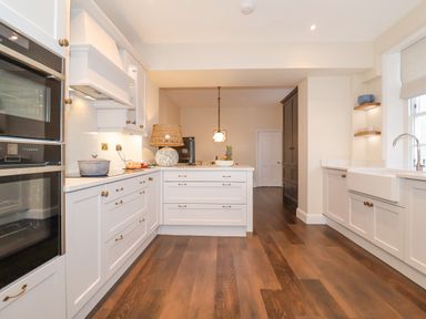 A kitchen with white cabinets wooden floor a lamp and a sink at The Middle House in Southwold