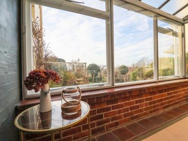 A room with large windows looking out to a garden with a table holding a vase of dried flowers and a glass jar at The Middle House in Southwold