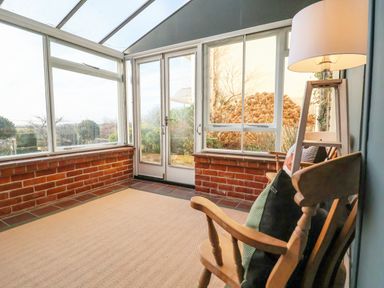A sunroom with wooden chairs and a floor lamp overlooking a garden at The Middle House in Southwold