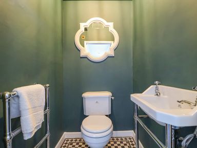 A bathroom with a toilet sink a towel rack with a white towel and a mirror on the wall at The Middle House in Southwold