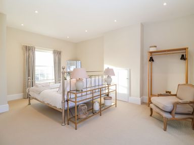 A bedroom with a metal bed frame white bedding two lamps on a table an armchair and an open clothing rack at The Middle House in Southwold