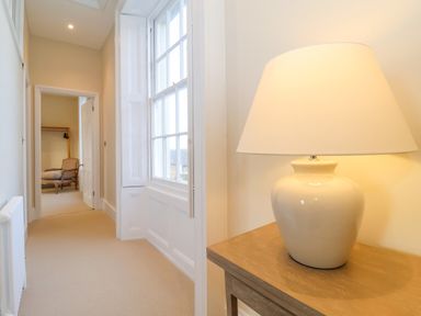 A hallway with a table lamp and a window showing a room with a chair at The Middle House in Southwold