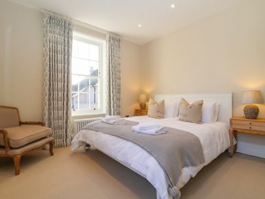 A bedroom with a double bed lamps on bedside tables an armchair and patterned curtains at The Middle House in Southwold