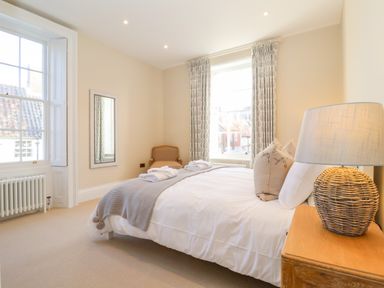 A bedroom with a bed side table lamp a chair two windows and a wall mirror at The Middle House in Southwold