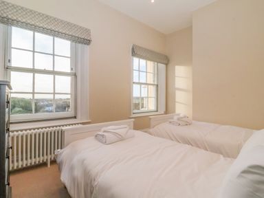 A bedroom with two single beds with folded towels on them and two windows with patterned blinds at The Middle House in Southwold