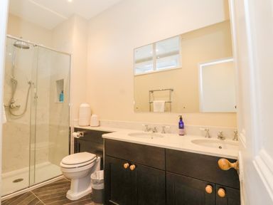 A bathroom with a glass shower enclosure dual sinks and a toilet at The Middle House in Southwold