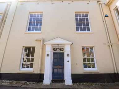 A blue door entrance with white frame and four windows on a beige building at The Middle House in Southwold