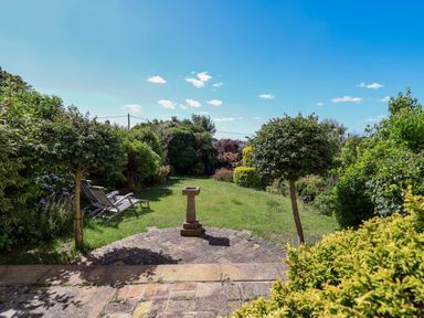 A garden with grass lawn two trees two wooden chairs and a stone birdbath at The Middle House in Southwold
