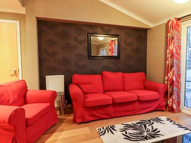 A living room with a red armchair and sofa a patterned rug and a mirror on a dark feature wall at Washburn Lodge in Fewston near Darley