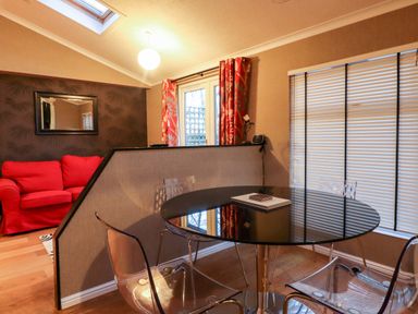 A dining area with a round black glass table and transparent chairs next to a room divider and a red sofa visible beyond the partition at Washburn Lodge in Fewston near Darley