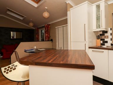 A kitchen area with wooden countertop and white cabinets next to a seating area with a red chair at Washburn Lodge Fewston near Darley