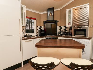 A kitchen with white cabinets black and white tiles a wooden island counter and two stools at Washburn Lodge in Fewston near Darley