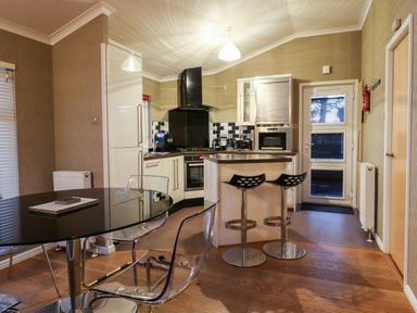 A kitchen with bar stools a round glass dining table and chairs at Washburn Lodge in Fewston near Darley