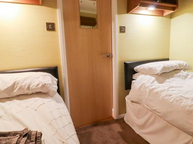 A small bedroom with two single beds a wooden door in between and wall-mounted shelves at Washburn Lodge Fewston near Darley