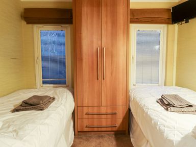 A bedroom with two single beds a wooden wardrobe between them and windows behind each bed at Washburn Lodge in Fewston near Darley