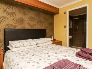 A bedroom with a double bed and patterned bedding and a doorway leading to a shower at Washburn Lodge in Fewston near Darley