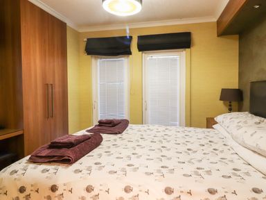 A bedroom with a bed covered in patterned bedding folded towels on the bed wooden wardrobes and a bedside table with a lamp at Washburn Lodge Fewston near Darley
