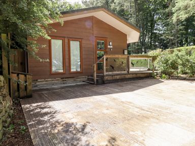 An exterior view of a wooden cabin with two windows and a glass-paneled porch surrounded by trees at Washburn Lodge Fewston near Darley