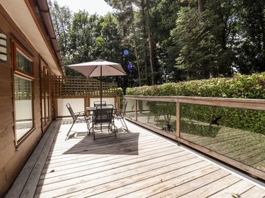 A wooden deck with a table and four chairs under a patio umbrella surrounded by trees at Washburn Lodge in Fewston near Darley