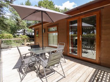 An outdoor wooden deck with a glass table and four chairs under a large umbrella at Washburn Lodge in Fewston near Darley