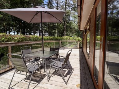 An outdoor wooden deck with a glass table and six chairs under a large umbrella at Washburn Lodge Fewston near Darley