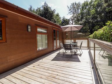 An outdoor wooden deck with a table umbrella and chairs surrounded by trees at Washburn Lodge in Fewston near Darley