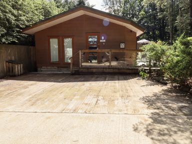 A brown wooden cabin with a small porch and glass door in a forested area at Washburn Lodge in Fewston near Darley