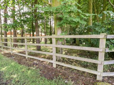 A wooden fence with trees and grass behind it at Washburn Lodge in Fewston near Darley