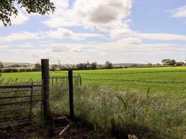 A fenced green field with trees and hills under a cloudy sky at Washburn Lodge in Fewston near Darley