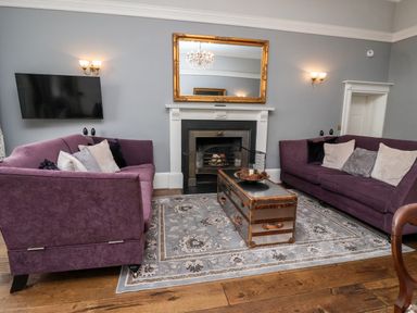 A living room with two purple sofas a fireplace a gold-framed mirror and a chest-style coffee table at The Stables and West Wing Bolton Percy near Tadcaster