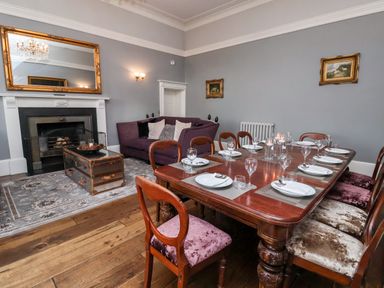 A dining room with a wooden table set for eight people and a purple sofa near a fireplace at The Stables and West Wing in Bolton Percy near Tadcaster